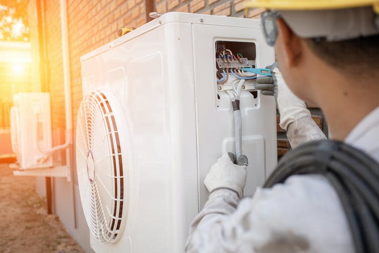 An engineer installing an air-source heat pump outside a house.