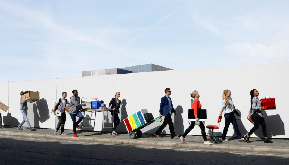 Office workers walking in a line down street carrying office equipment