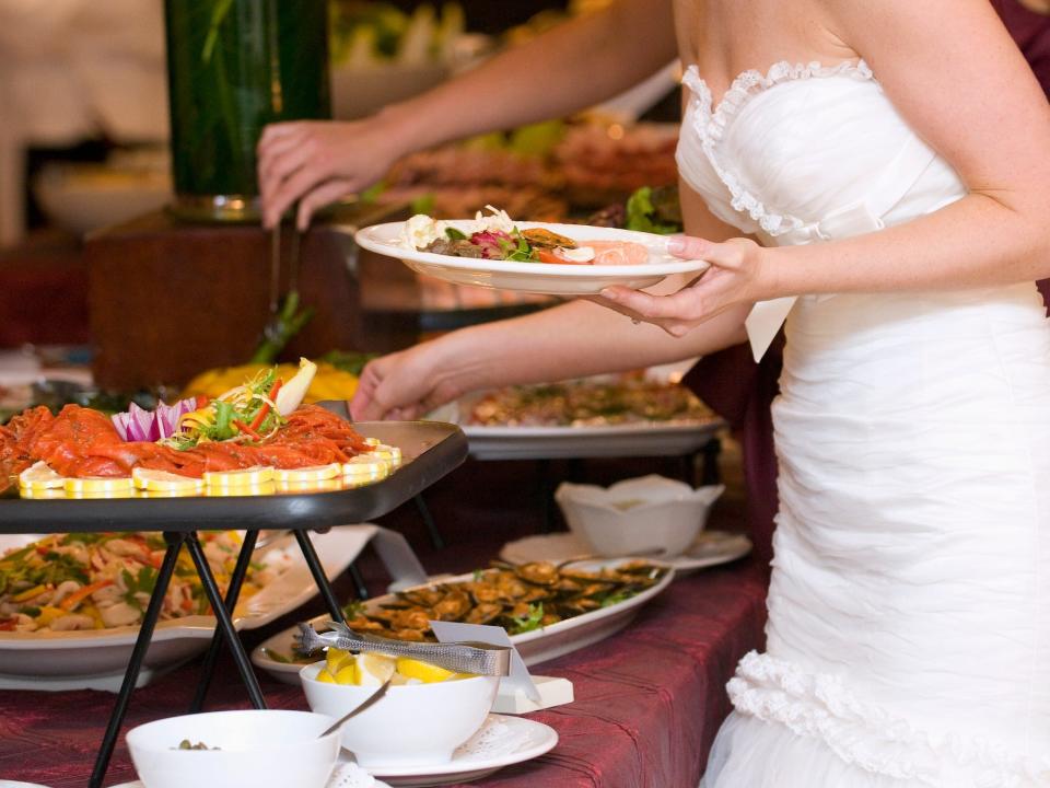 A bride serves herself at a buffet at her wedding.