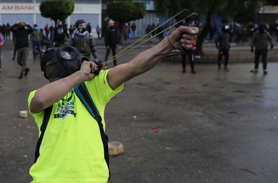 A protester fires a slingshot towards riot policemen during a protest against deteriorating living conditions and strict coronavirus lockdown measures, in Tripoli, north Lebanon, Thursday, Jan. 28, 2021. Violent confrontations for three straight days between protesters and security forces in northern Lebanon left a 30-year-old man dead and more than 220 people injured, the state news agency said Thursday. (AP Photo/Hussein Malla)