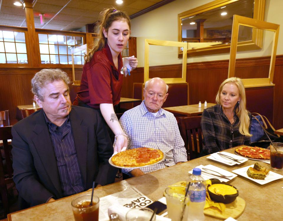 Christopher Knight, left, who played Peter Brady in the TV classic "The Brady Bunch," is served a bar pizza by waitress Morgan Beatty while eating at the Cape Cod Cafe in Brockton with Jimmy Jamoulis, center, a co-owner of the restaurant, and his wife, Cara Knight, right, on Tuesday, May 2, 2023.