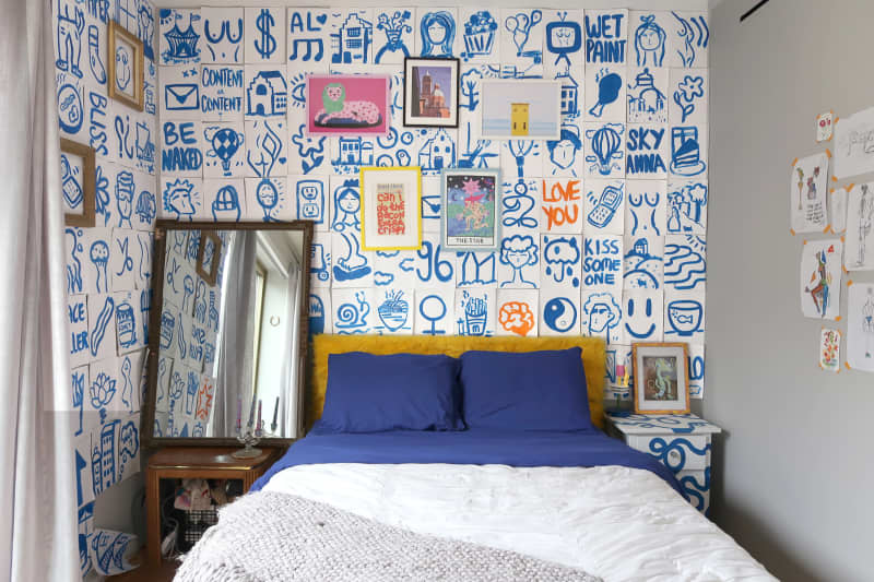 Bedroom with white wall behind bed with blue drawings and words
