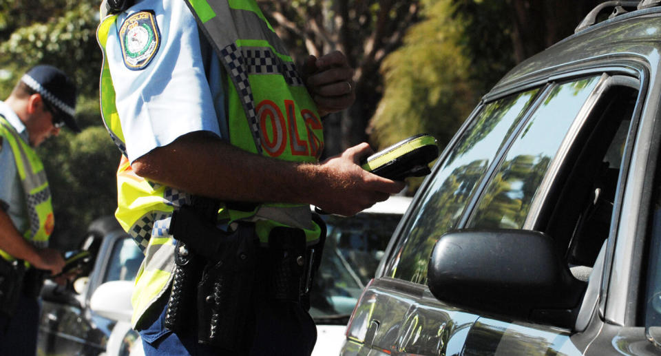 A stock photo of a NSW Police officer next to a stationary car. Drivers in NSW will be handed double demerit points over the Queen's Birthday long weekend.