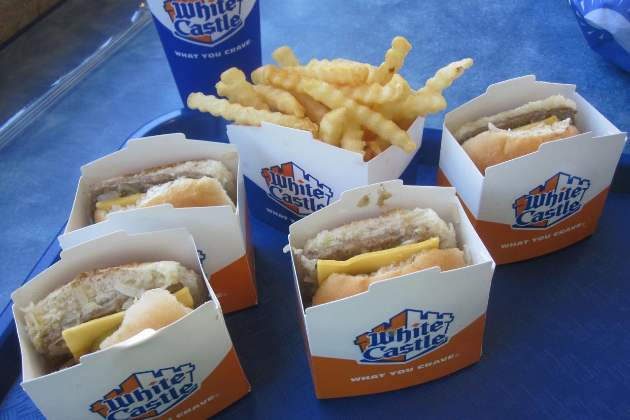 Four White Castle Cheese Sliders with fries in serving boxes and a drink on a blue table