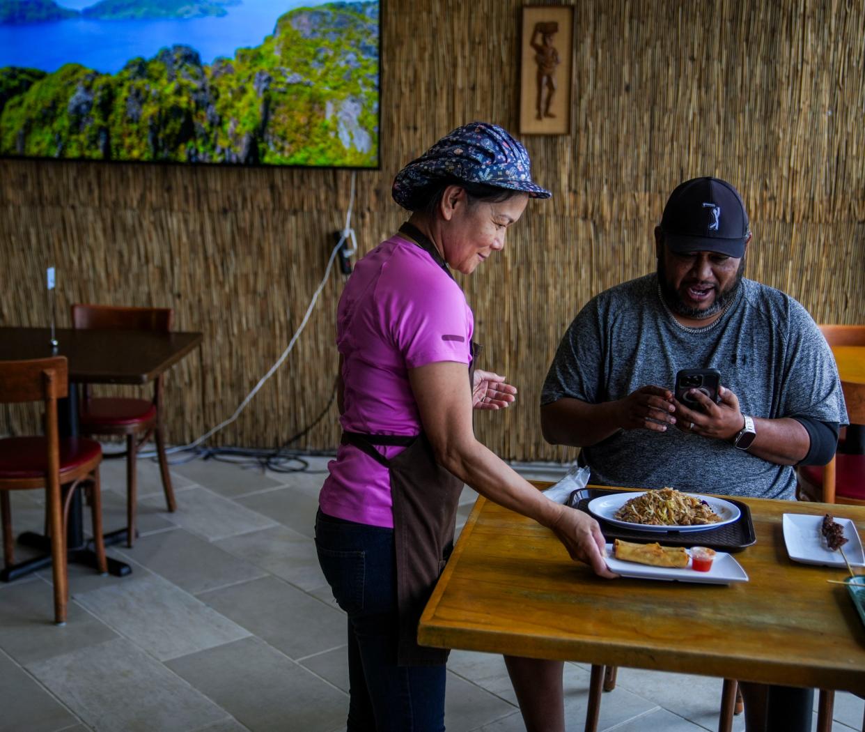 Cook Yollie Olivares hands a dish to a customer Thursday, July 25, 2024, at Yollie’s, a new restaurant at the Philippine Cultural Community Center in Indianapolis.