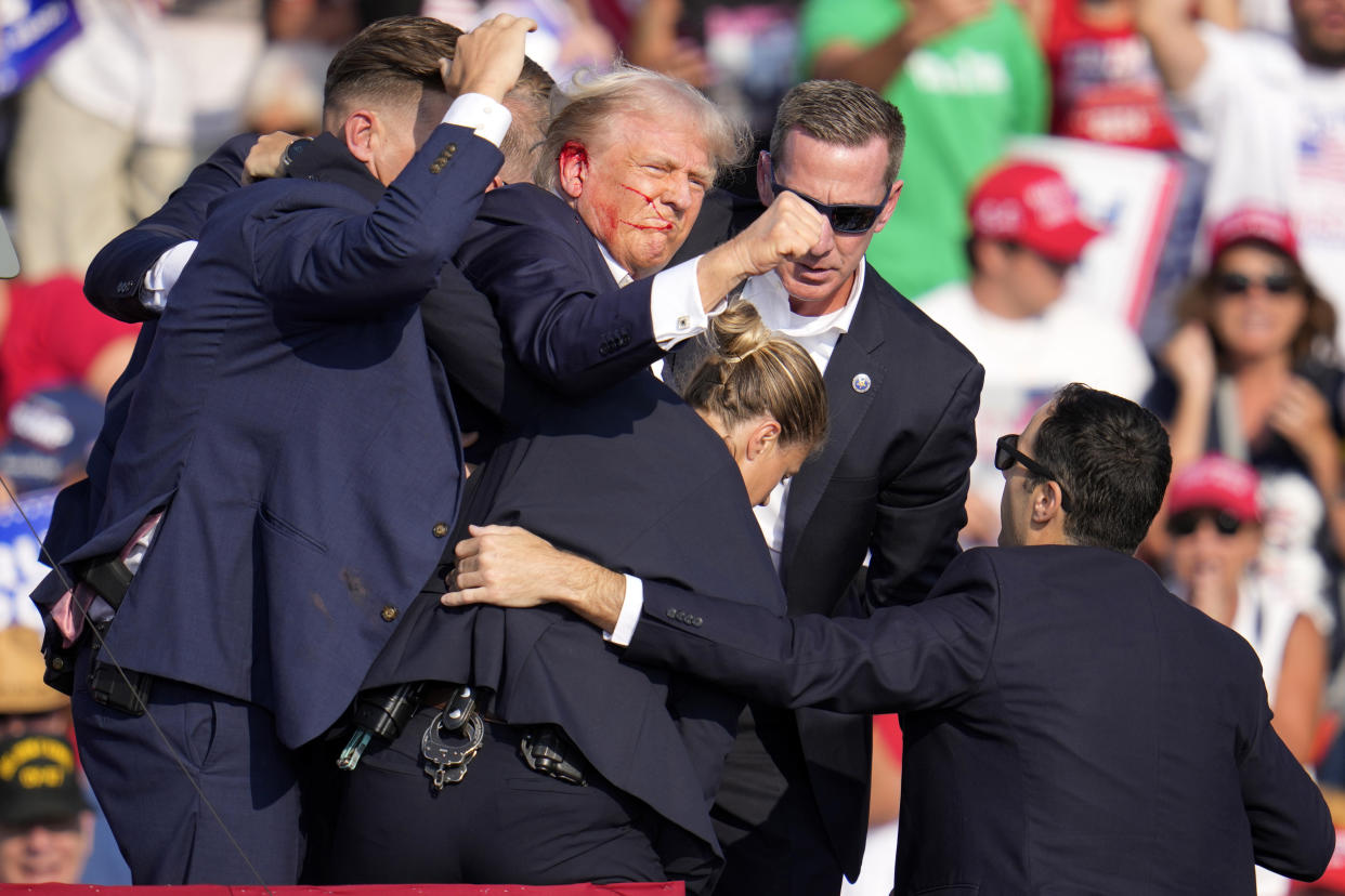 Trump, apparently bleeding near his right ear and attempting to hoist his fist, is helped off the stage by U.S. Secret Service.