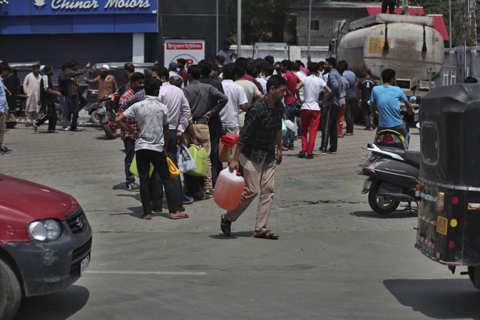 A Kashmiri man walks carrying fuel as other residents queue up at a fuel station in Srinagar, India, Sunday, Aug. 4, 2019. People in Srinagar and other towns in Indian kashmir thronged grocery stores and medical shops to stock up on essentials. Tensions have soared along the volatile, highly militarized frontier between India and Pakistan in the disputed Himalayan region of Kashmir as India deployed more troops and ordered thousands of visitors out of the region. (AP Photo/Mukhtar Khan)