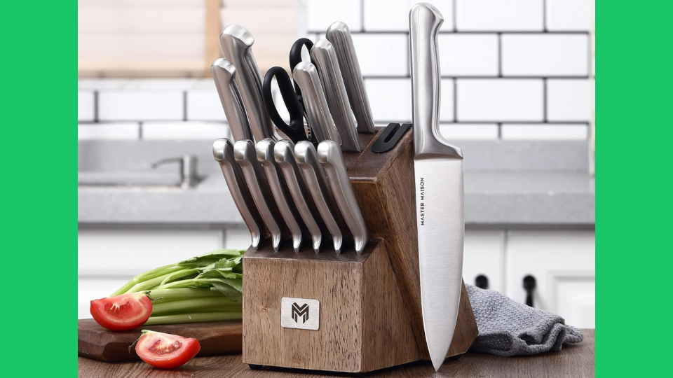 the silver knives in a wooden block next to tomatoes and greens on a table