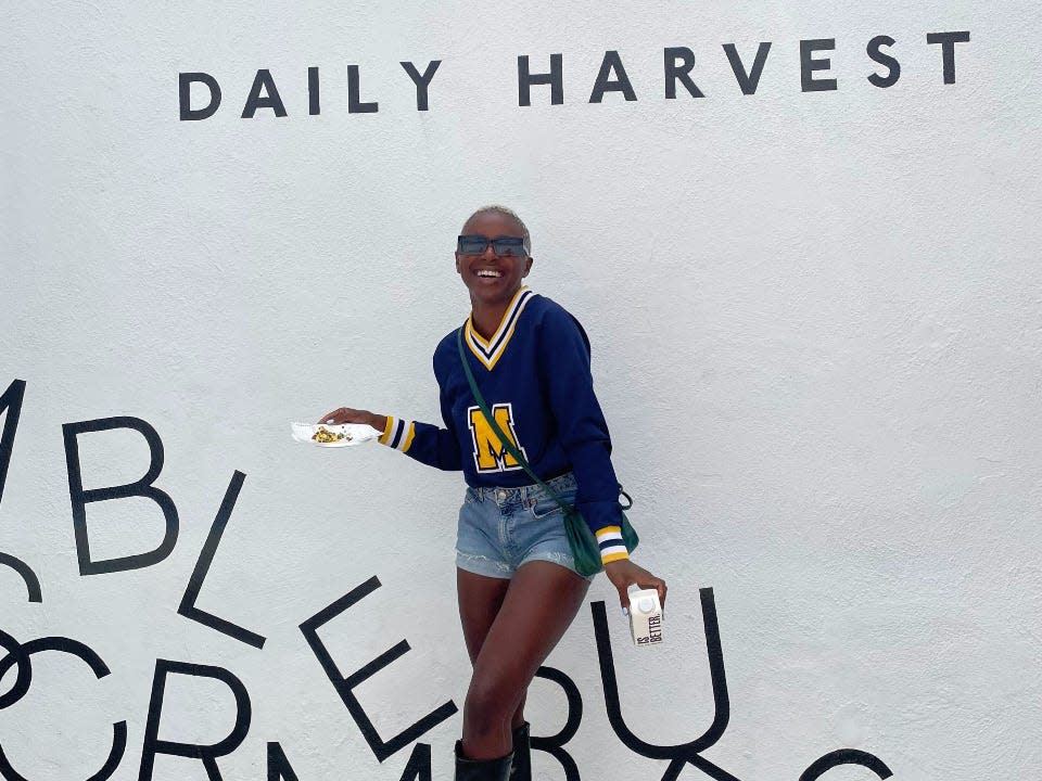 Influencer Ashley Stuart trying a sample of a Daily Harvest food in front of a "Daily Harvest" sign and letters reading "crumbles" at a pop-up event