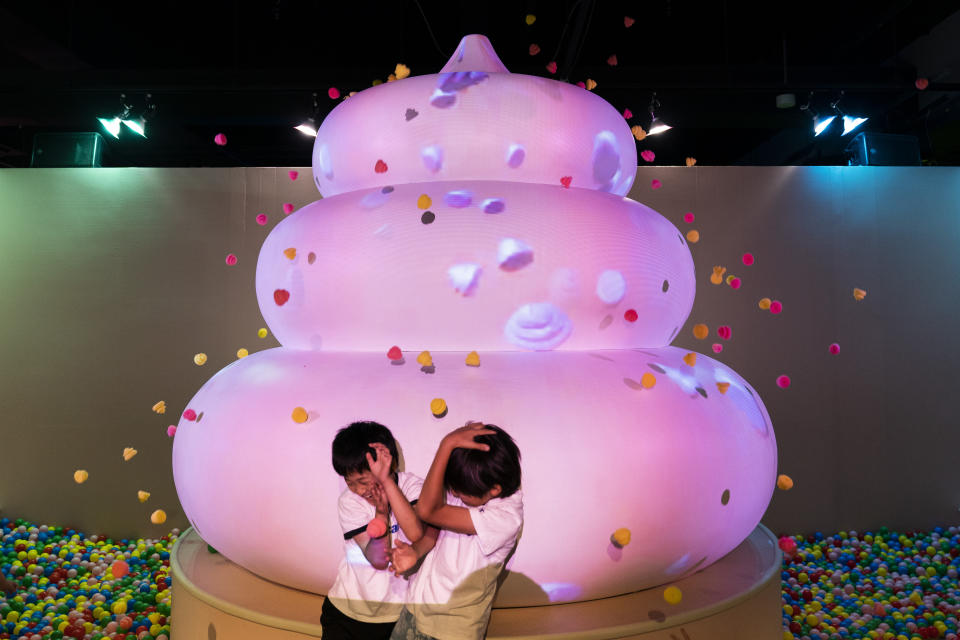 In this Tuesday, June 18, 2019, photo, two boys jokingly take cover as small toy poops gush from a giant poop-shaped inflatable at the Unko Museum in Yokohama, south of Tokyo. In a country known for its cult of cute, even poop is not an exception. A pop-up exhibition at the Unko Museum in the port city of Yokohama is all about unko, a Japanese word for poop. The poop installations there get their cutest makeovers. They come in the shape of soft cream, or cupcake toppings. (AP Photo/Jae C. Hong)