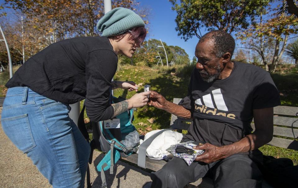 A woman hands out Narcan to a man at Tongva Park in Santa Monica