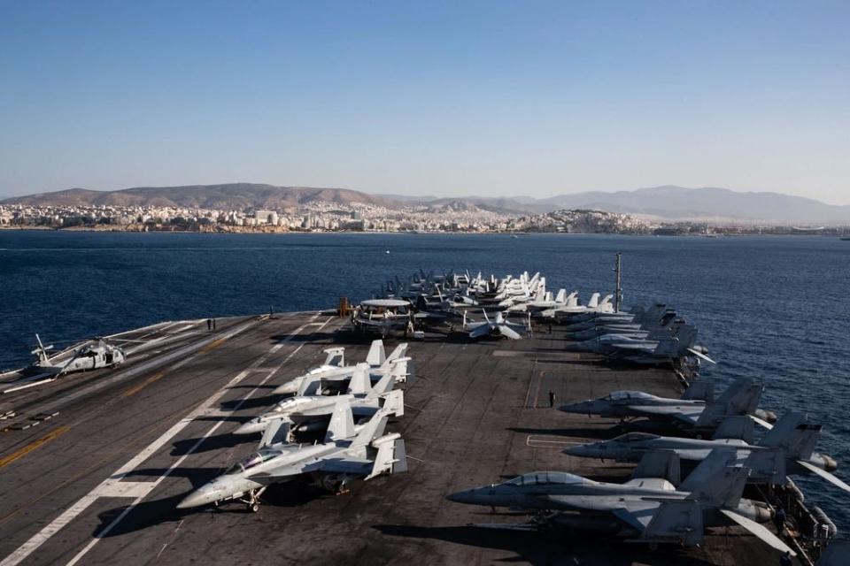 aircraft are seen on the flight deck of an military aircraft carrier with the coast of greece visible in the horizon