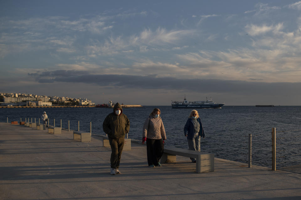 Pedestrian wearing face masks to curb the coronavirus walk by the sea at Lipasmata Multifunctional Park in Drapetsona suburb of Piraeus, near Athens, on Monday, Nov. 23, 2020. A second nationwide lockdown was imposed earlier this month until the end of November but the restrictions are widely expected to be extended into December in some form. (AP Photo/Petros Giannakouris)