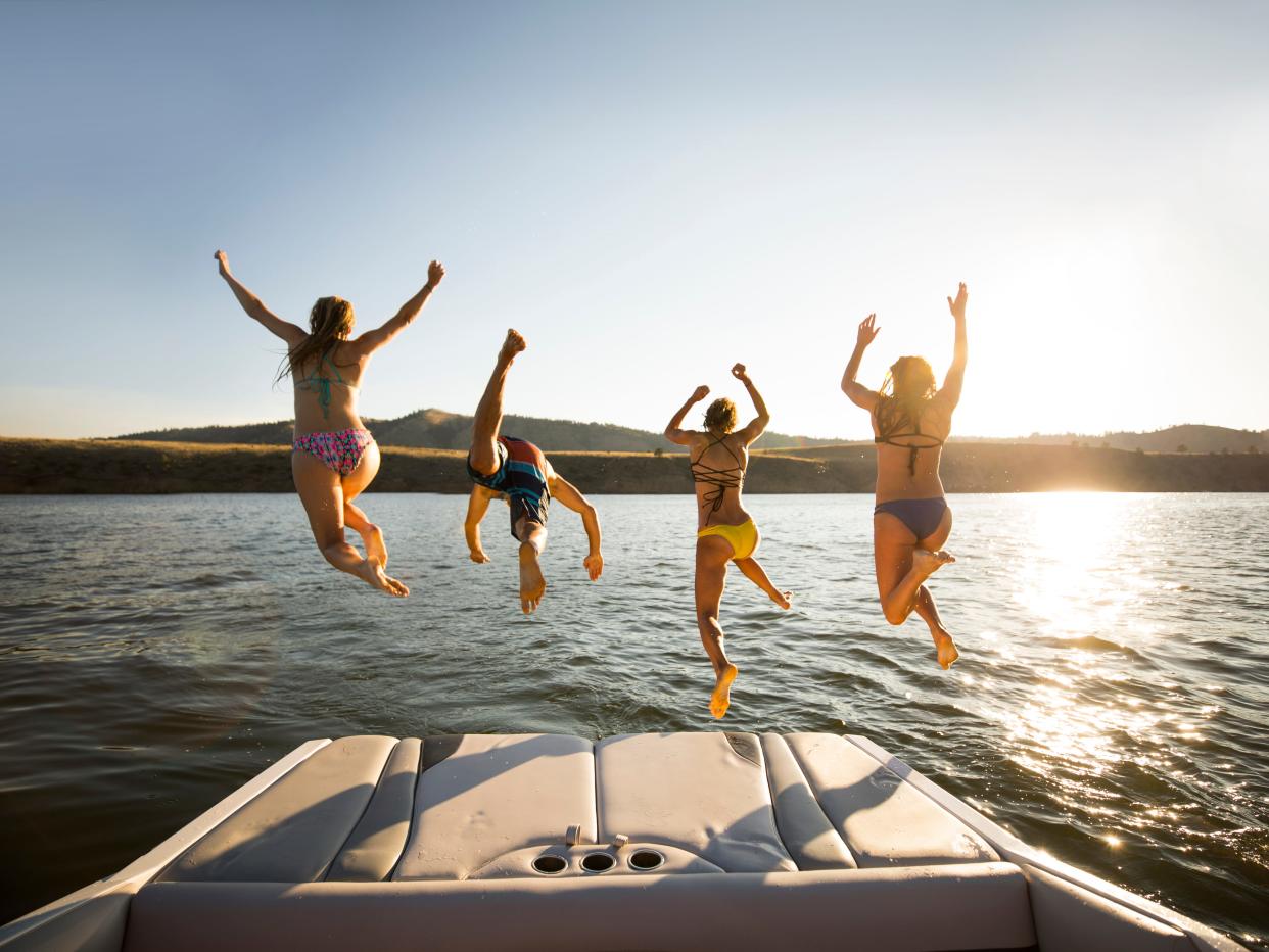 a group of young people in bathing suits jumping off of the back of a boat into the water with their hands up