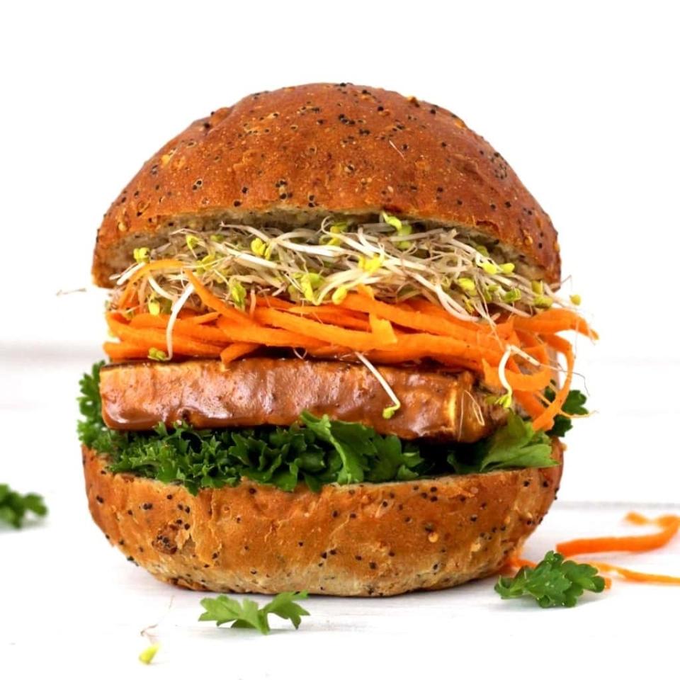 A gourmet vegan sandwich with a seeded bun, leafy greens, a thick patty, shredded carrots, and sprouts