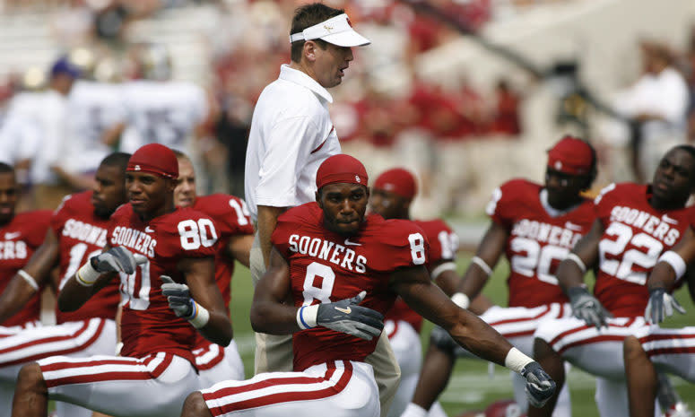 Bob Stoops walking by his players as they stretch.