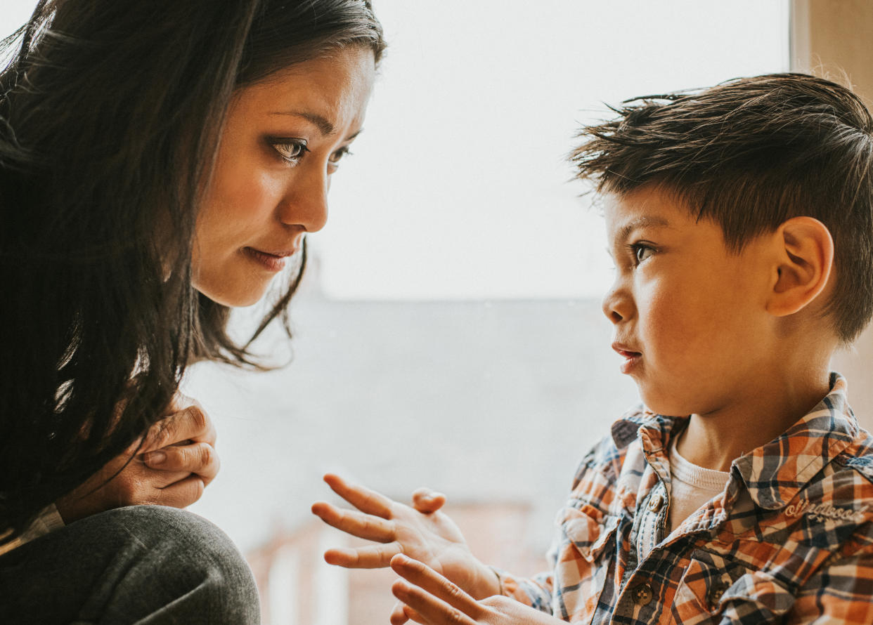 A boy gestures using his hands. A woman, who sits close-by, listens and watches him intently 