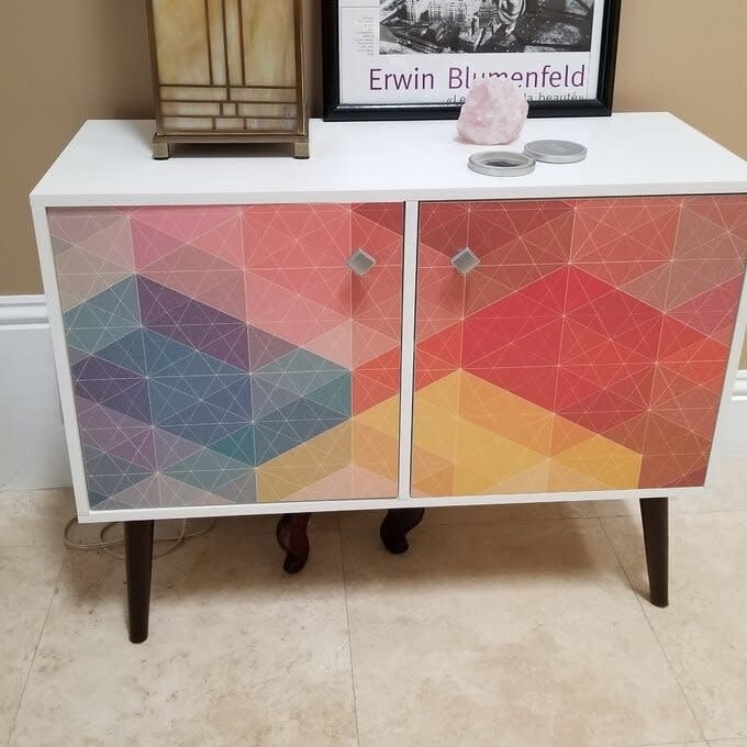 A cabinet with geometric patterned doors in a room with decor items and a framed picture above