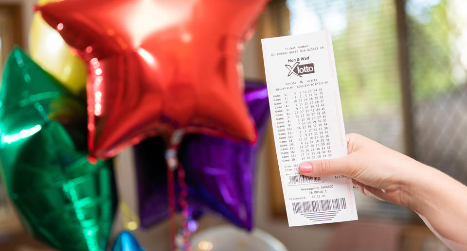 A woman holds a Monday & Wednesday X Lotto ticket in front of a bunch of colourful balloons.