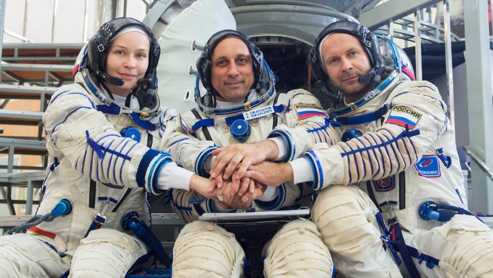 Three cosmonauts sitting together in space suits holding hands