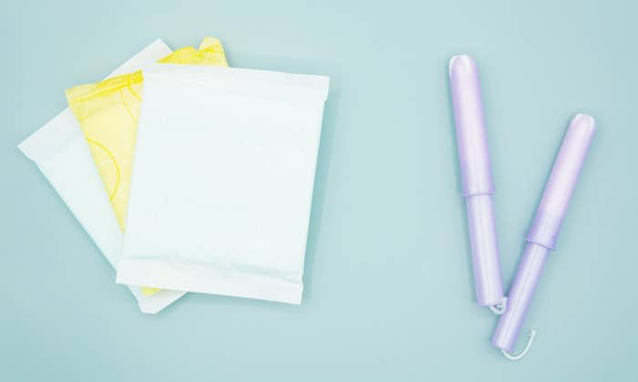 Two sanitary pads in their packaging are on the left, and two tampons with applicators are on the right against a plain background