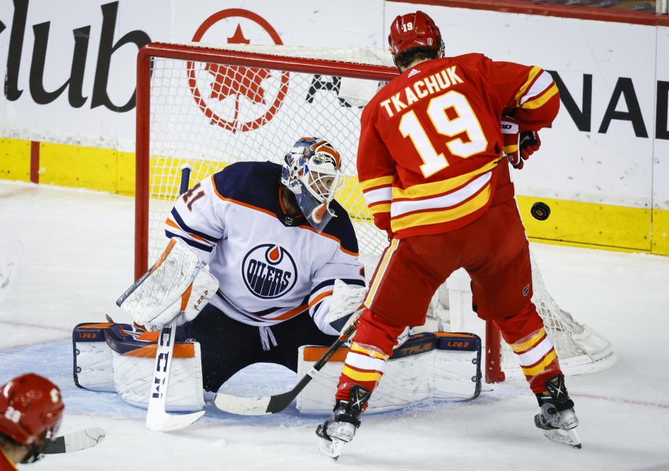 Edmonton Oilers goalie Mike Smith, left, deflects a shot wide of the net as Calgary Flames' Matthew Tkachuk looks for a rebound during the second period of Game 5 of an NHL hockey second-round playoff series Thursday, May 26, 2022, in Calgary, Alberta. (Jeff McIntosh/The Canadian Press via AP)