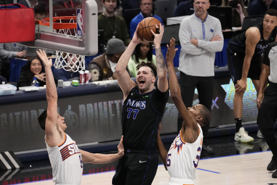 Dallas Mavericks guard Luka Doncic (77) leaps to the basket to take a shot as Phoenix Suns' Grayson Allen, left, and Kevin Durant, right, defend in the first half of an NBA basketball game in Dallas, Wednesday, Jan. 24, 2024. (AP Photo/Tony Gutierrez)