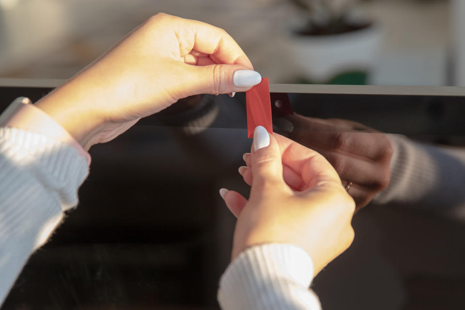 A woman places a strip of red tape over a webcam on her monitor