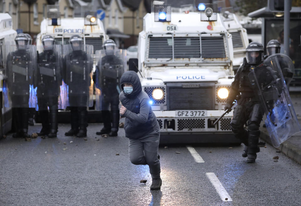 A Nationalist youth runs away after throwing a projectile at a police line blocking a road near the Peace Wall in West Belfast, Northern Ireland, Thursday, April 8, 2021. Authorities in Northern Ireland sought to restore calm Thursday after Protestant and Catholic youths in Belfast hurled bricks, fireworks and gasoline bombs at police and each other. It was the worst mayhem in a week of street violence in the region, where Britain's exit from the European Union has unsettled an uneasy political balance. (AP Photo/Peter Morrison)