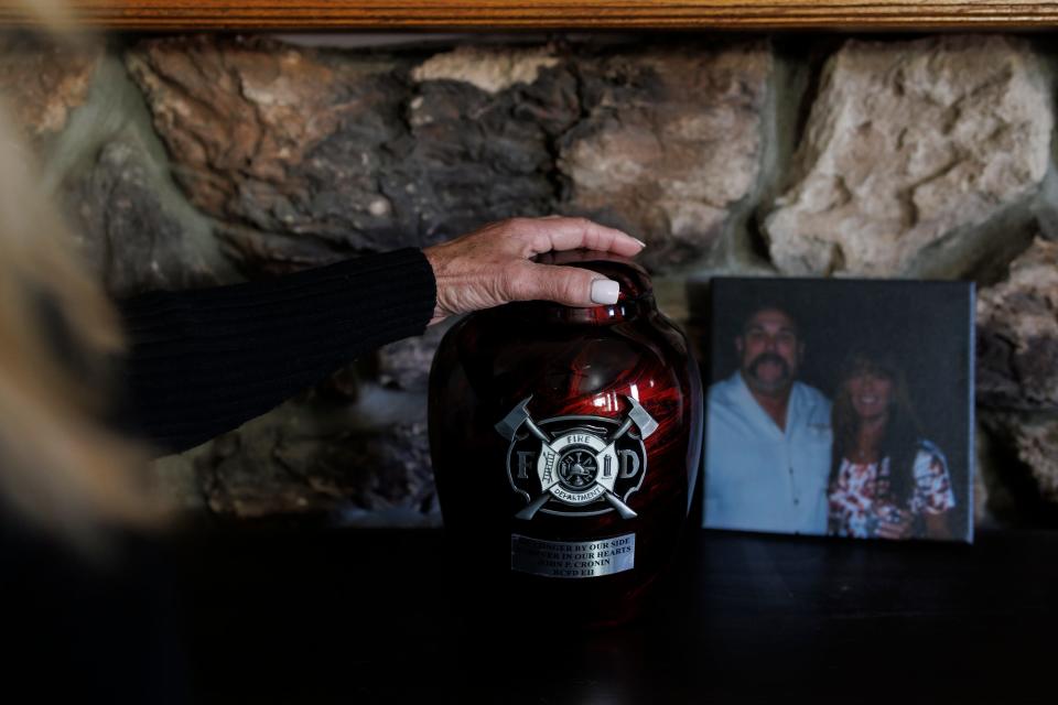 Jocelyn Cronin puts her hand on her husband's urn at the altar she made in his memory in her home in Petaluma, California.