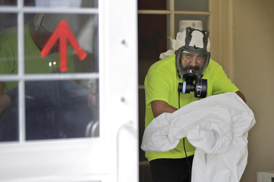 A member of a cleaning crew removes his protective gear after sanitizing a bank in New Rochelle, N.Y., Wednesday, March 11, 2020. State officials are shuttering several schools and houses of worship for two weeks in the New York City suburb and sending in the National Guard to help with what appears to be the nation's biggest cluster of coronavirus cases, Gov. Andrew Cuomo said Tuesday. (AP Photo/Seth Wenig)