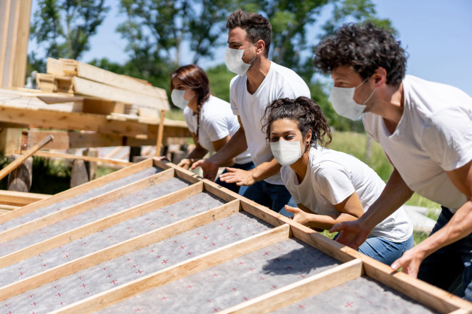 Group of Latin American volunteers building a house fo charity while wearing a facemask during the COVID-19 pandemic