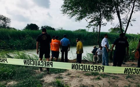 Authorities stand behind yellow warning tape along the Rio Grande bank where the bodies were found