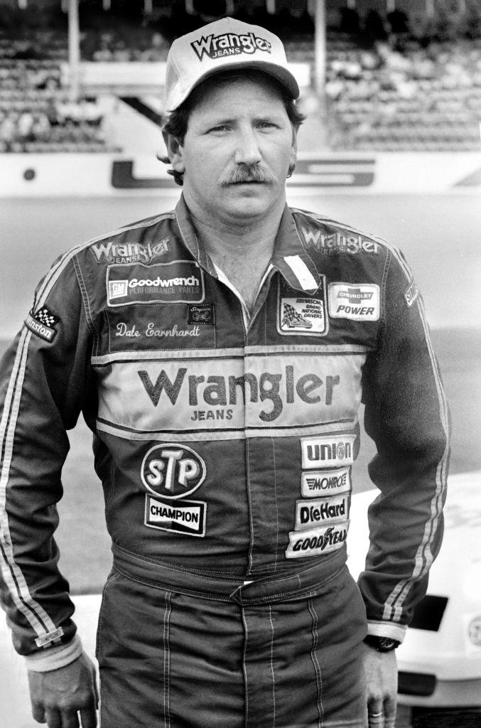 Dale Earnhardt stands confidently in racing gear with sponsor logos, at a racetrack