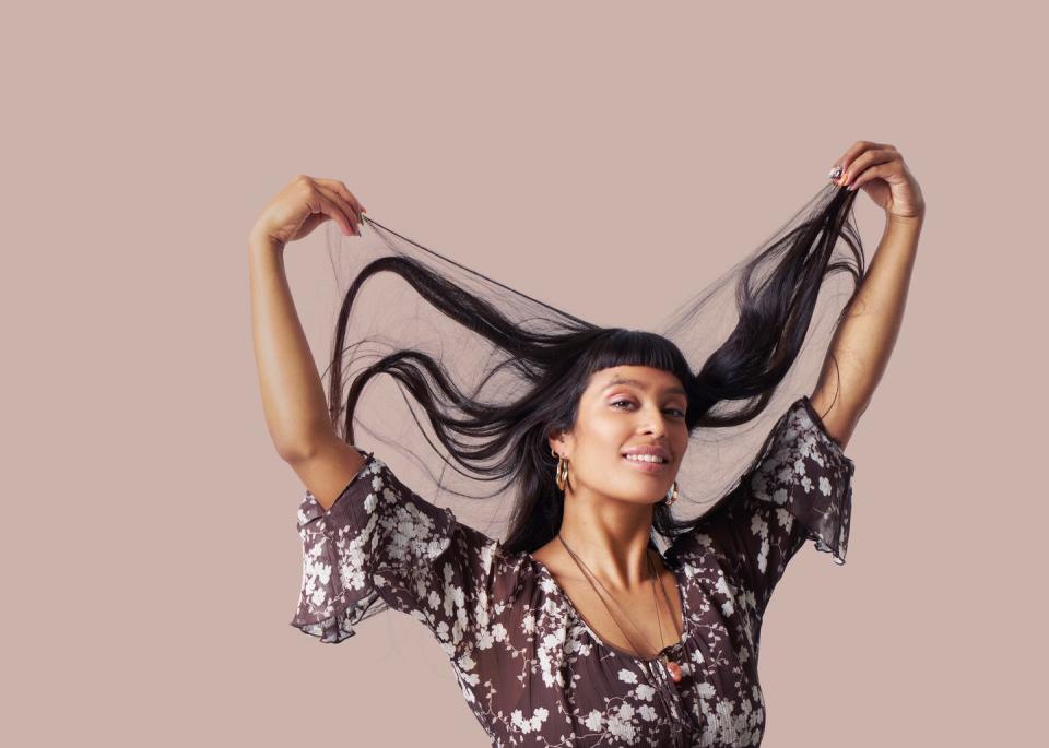 Studio shot of a young woman holding up strands of her long hair and smiling at the camera