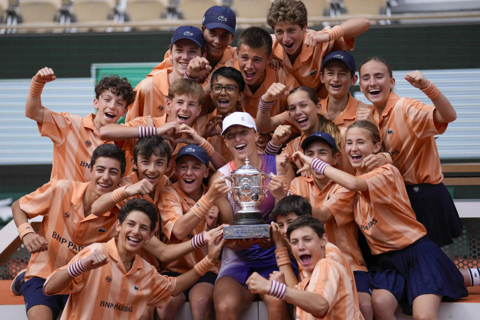 Ball kids pose with Poland's Iga Swiatek who holds the trophy after winning the women's final of the French Open tennis tournament against Italy's Jasmine Paolini at the Roland Garros stadium in Paris, France, Saturday, June 8, 2024. (AP Photo/Thibault Camus)