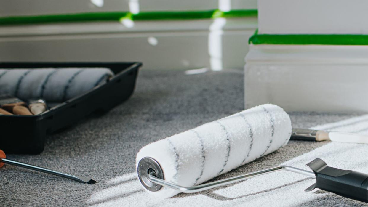  A clean paint roller on the floor in front of a wall with painters tape 