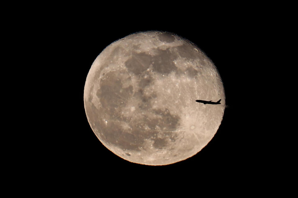 A passenger plane passes in front of the full Pink moon as rises over Manhattan in New York City, United States on April 17, 2022. / Credit: Tayfun Coskun/Anadolu Agency via Getty Images