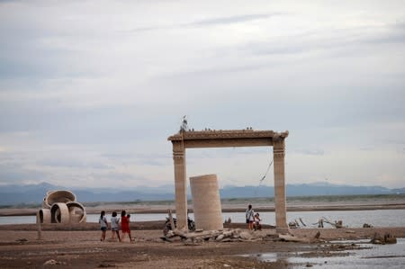 People walk through the ruins of an old Buddhist temple, which has resurfaced in a dried-up dam due to drought, in Lopburi, Thailand