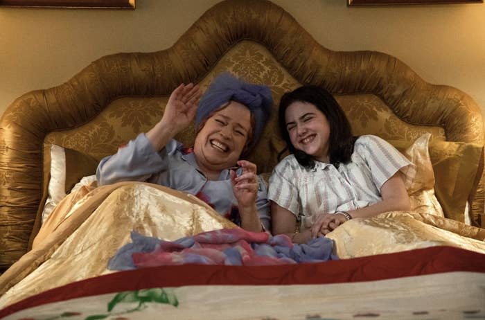 Kathy Bates and Joey King are in bed, laughing together. Kathy is wearing a nightgown and headwrap, and Joey is in pajamas