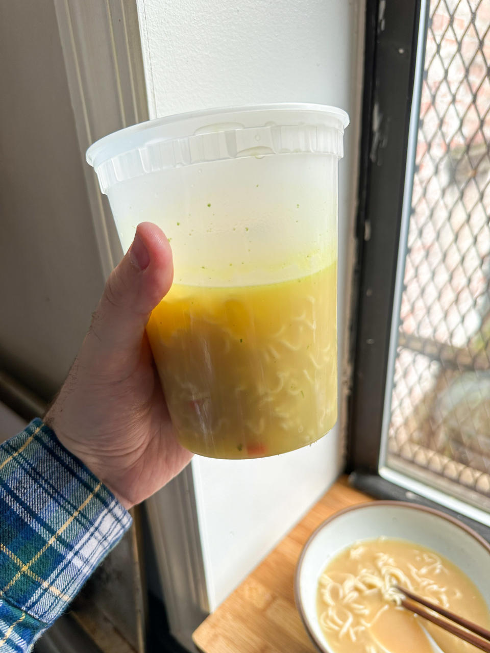 quart plastic deli container in author's hand, holding up various packages of cooked ramen combined