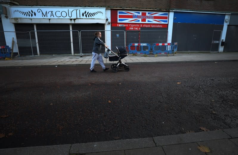 Woman pushes a pram past boarded up retail units in the centre of Crewe