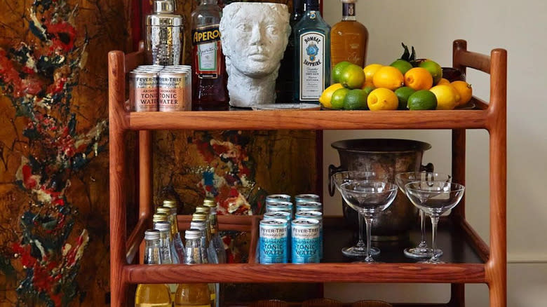 bar cart with alcohol, tonic, glasses, lemons and limes