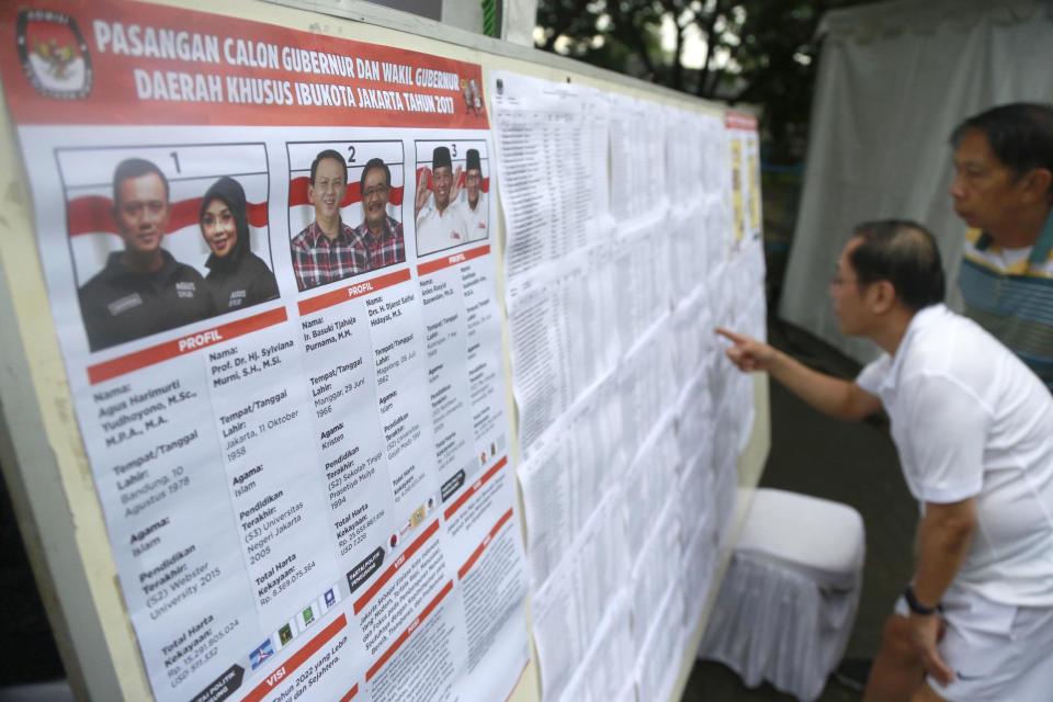 Men inspect a list of voters put up along with a poster of candidates at a polling station in Jakarta, Indonesia, Wednesday, Feb. 15, 2017. Voting was underway in the election for governor of the Indonesian capital after a divisive months-long campaign in which the monumental problems facing Jakarta took a backseat to religious intolerance and racial bigotry. (AP Photo/Dita Alangkara)