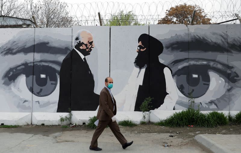 FILE PHOTO: An Afghan man wearing a protective face mask walks past a wall painted with photo of Zalmay Khalilzad, U.S. envoy for peace in Afghanistan, and Mullah Abdul Ghani Baradar, the leader of the Taliban delegation, in Kabul