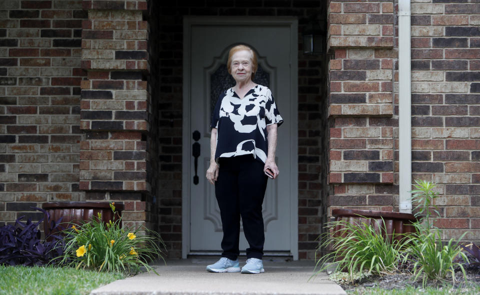 Dell Kaplan, 81, stands for a photo in front of her home in Plano, Texas Friday, May 15, 2020. For Kaplan, the offer to get calls from a stranger just to chat while staying home during the coronavirus pandemic was immediately appealing. "It gets pretty lonely here by yourself," said Kaplan, a suburban Dallas resident who has been missing meals out with friends, family get-togethers and going to classes at a nearby college. The program being offered by the city of Plano is among those that have popped up across the U.S. during the pandemic to help older adults with a simple offer to engage in small talk. (AP Photo/LM Otero)