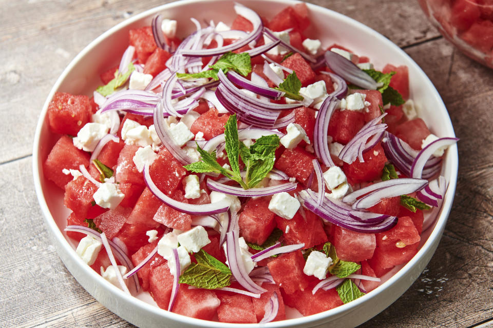 This image shows a recipe for watermelon feta salad topped with thinly sliced red onion and mint leaves. (Cheyenne Cohen via AP)