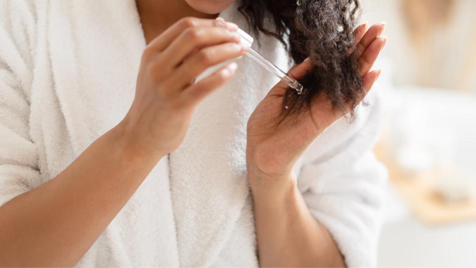 Woman applying a hair oil/serum to the ends of her curly hair, whilst wearing a towelled dressing gown