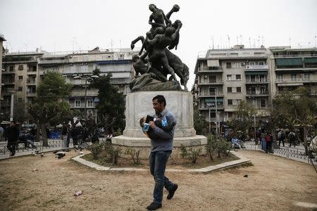 A stranded Afghan migrant carries his baby next to a statue depicting ancient Greek mythical hero Theseus saving Hippodameia from the centaur Eurytion, on Victoria square in Athens, Greece, February 24, 2016. REUTERS/Alkis Konstantinidis