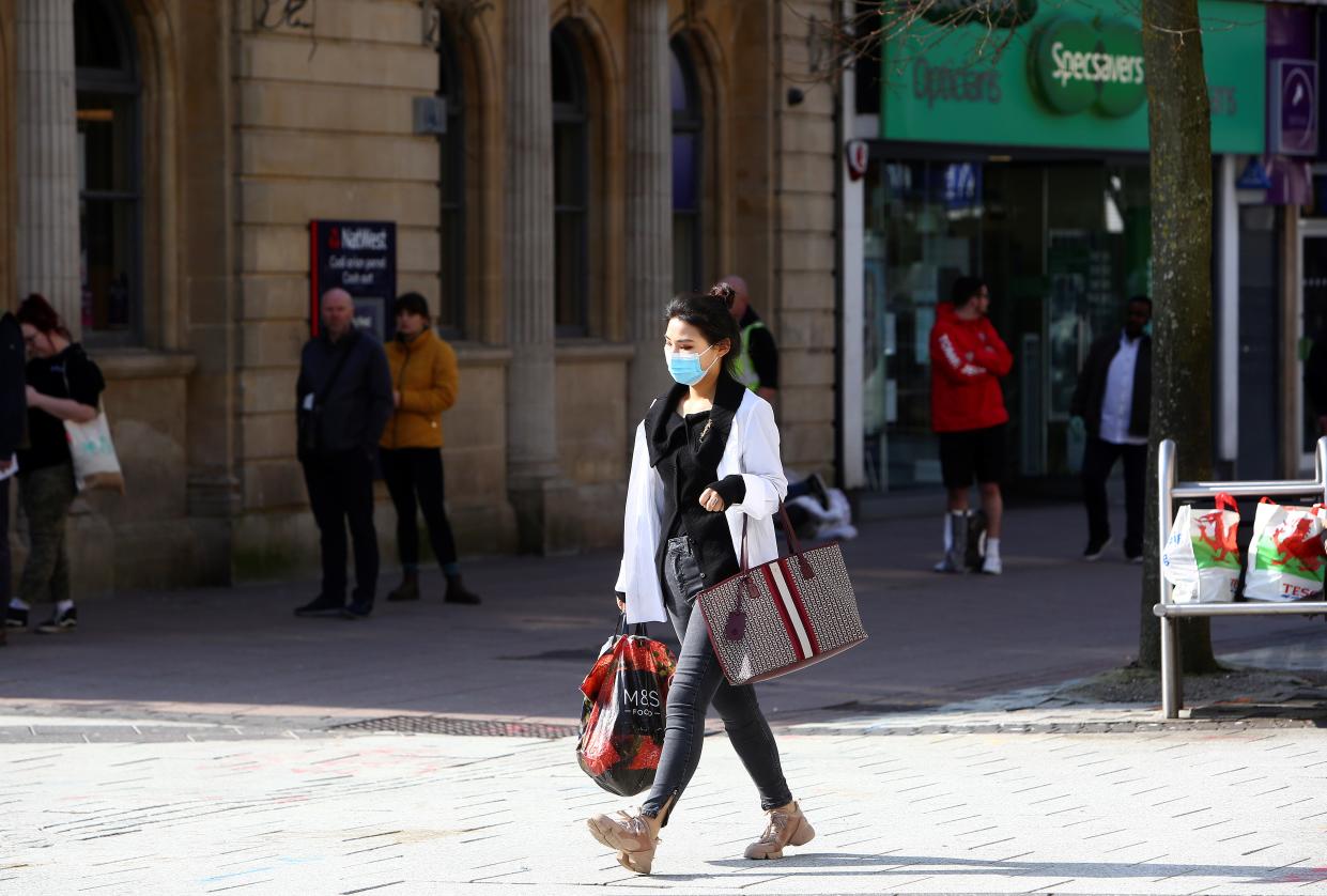 A woman, wearing a face mask as a precautionary measure against covid-19, as people stand at a distance and queue to enter a bank in Cardiff, south Wales on the morning on March 24, 2020 after Britain's government ordered a lockdown to slow the spread of the novel coronavirus. - Britain was under lockdown March 24, its population joining around 1.7 billion people around the globe ordered to stay indoors to curb the "accelerating" spread of the coronavirus. (Photo by GEOFF CADDICK / AFP) (Photo by GEOFF CADDICK/AFP via Getty Images)